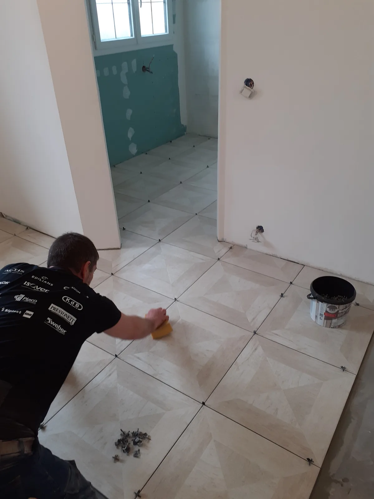 Luis Morais à genoux, en train de nettoyer les joints d'un carrelage grand format posé en diagonale